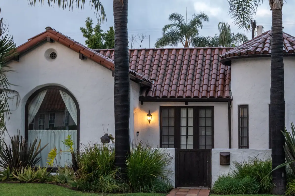 A white stucco home with a red clay tile roof and arched windows under tall palm trees