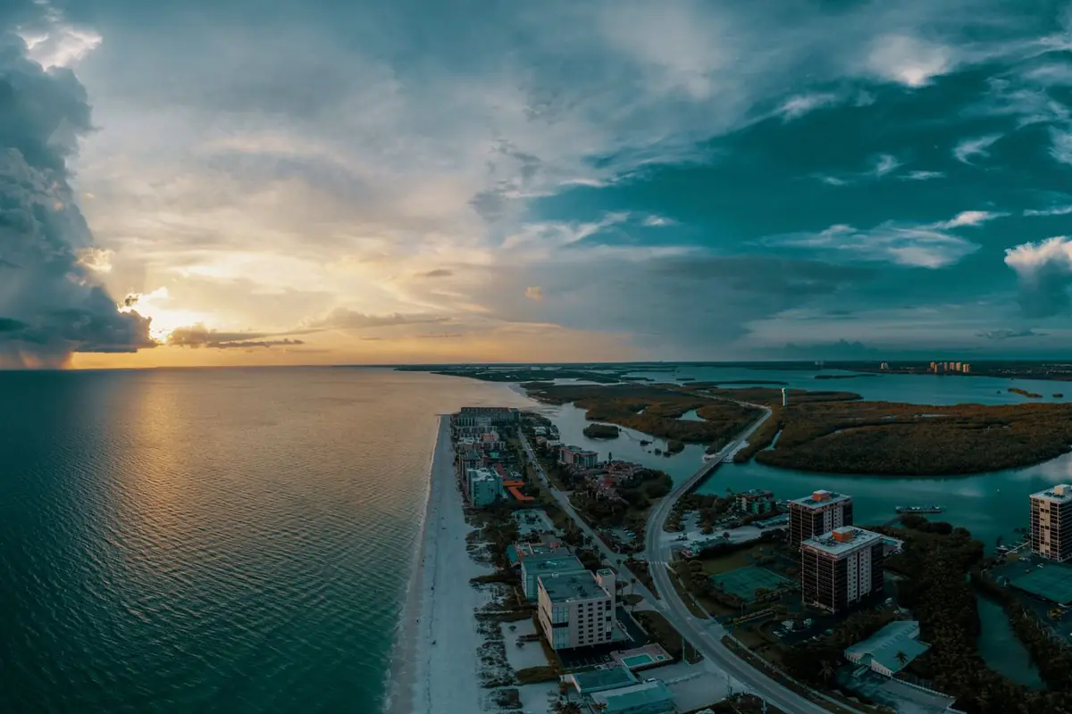 Aerial view at dusk of a narrow barrier island lined with beachfront buildings between the Gulf and a bay