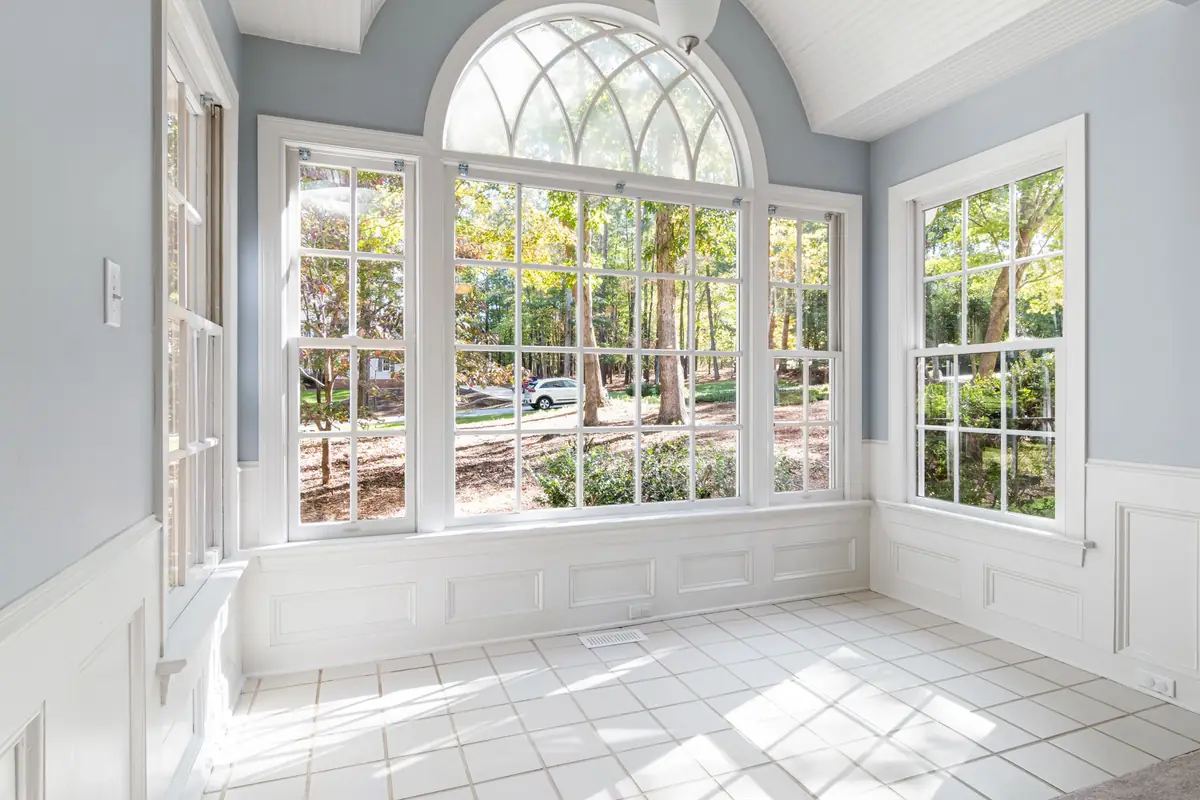 A bright sunroom with a wall of white-framed windows and an arched transom looking onto trees